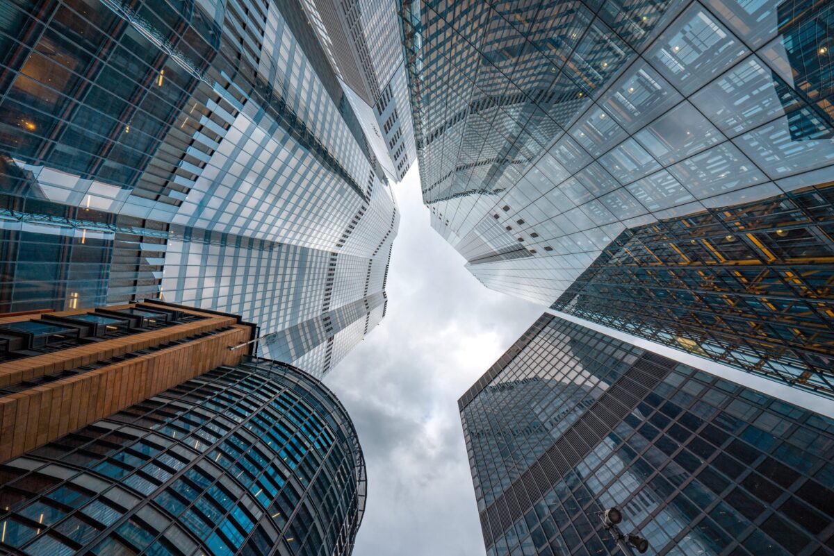 A view looking up to a cloudy sky between multiple glass skyscrapers.